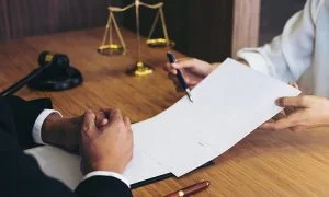 Contract handed across a desk with scales and a gavel